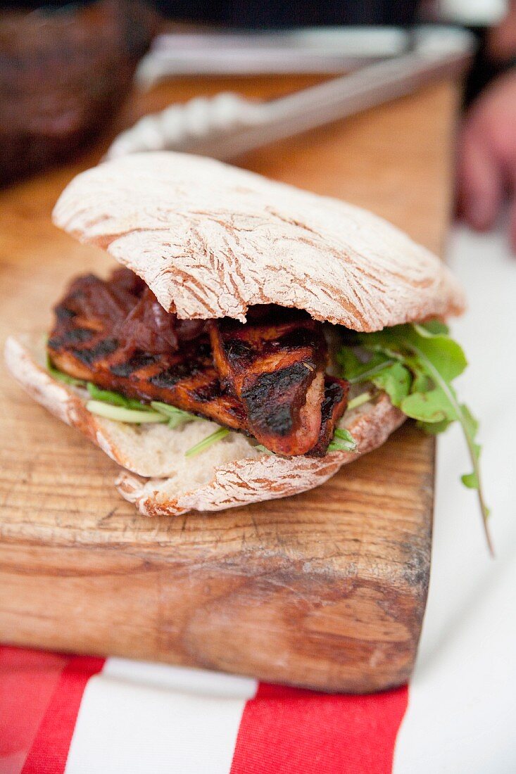 A grilled meat sandwich on a wooden board