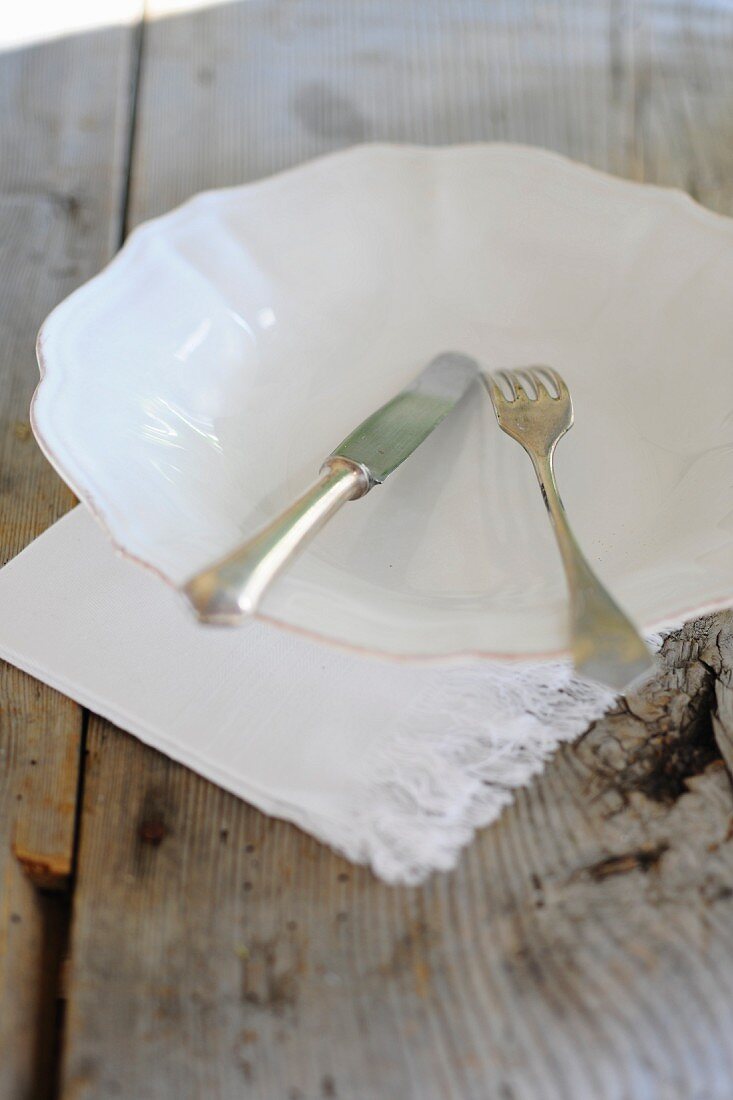 A white plate and cutlery with a napkin on a wooden table