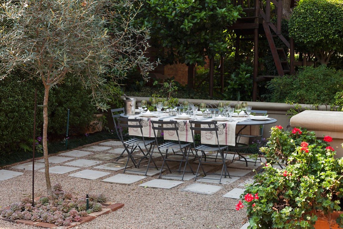 Set table in garden on gravel terrace with stone flags below trees