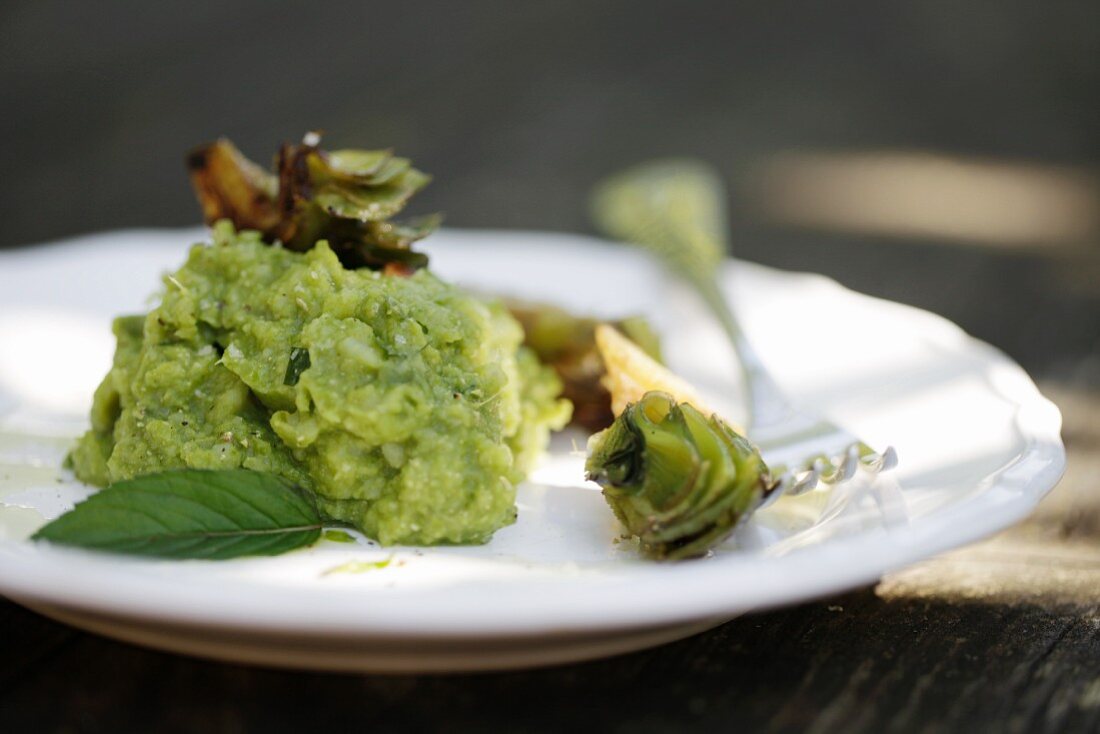 Pea and mint purée with fried artichokes on a white plate with a fork