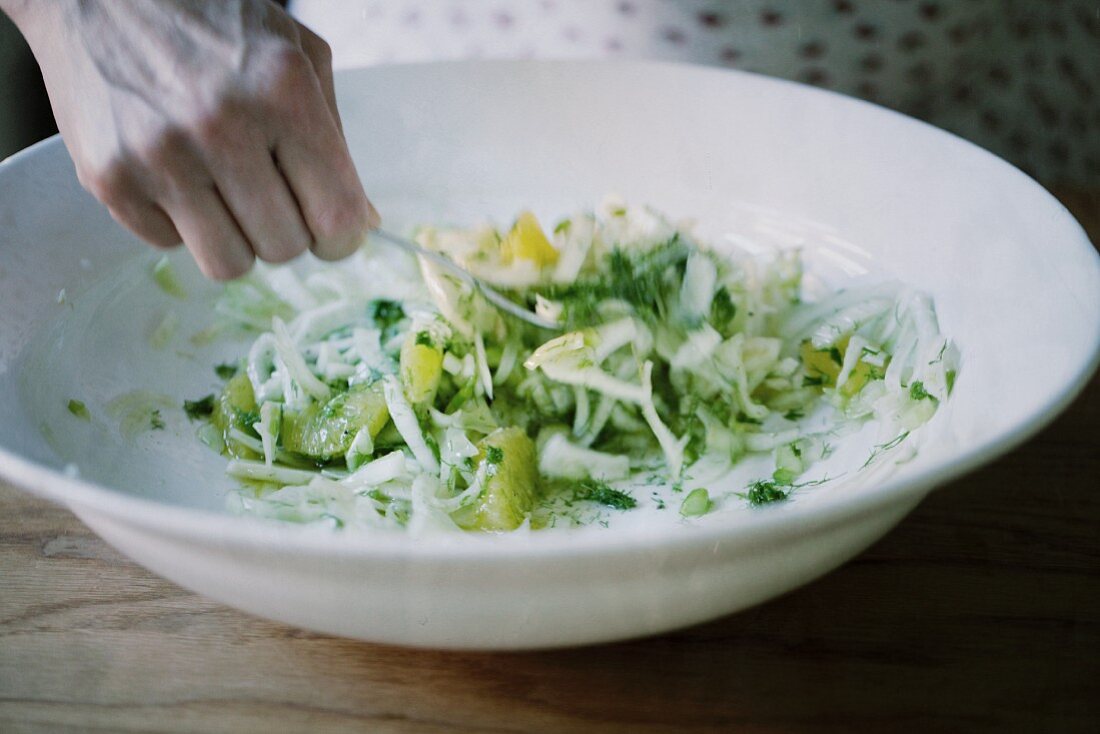 A hand mixing a fennel salad
