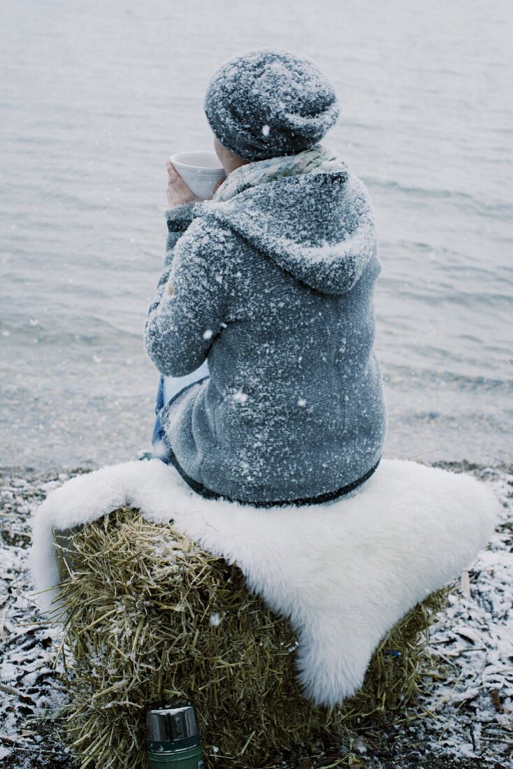 Frau mit Teetasse im Schnee am Seeufer