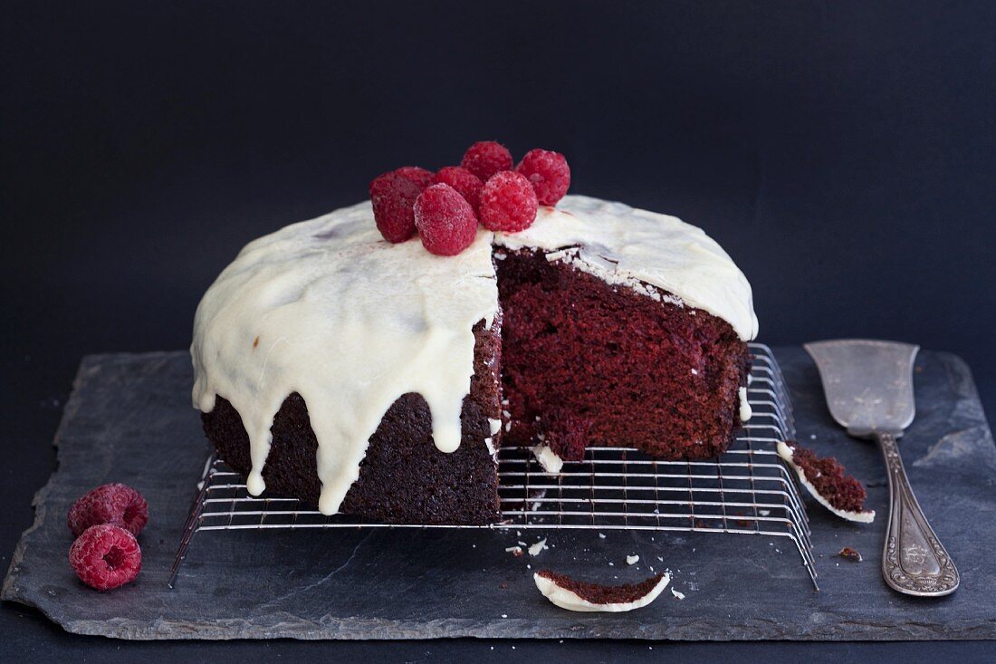 Red Velvet Cake mit Zuckerguss und Himbeeren auf Kuchengitter (angeschnitten)