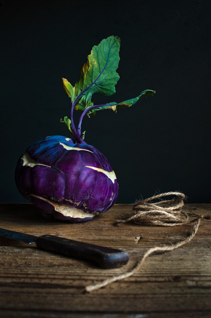 Purple kohlrabi with a knife and twine on a wooden table