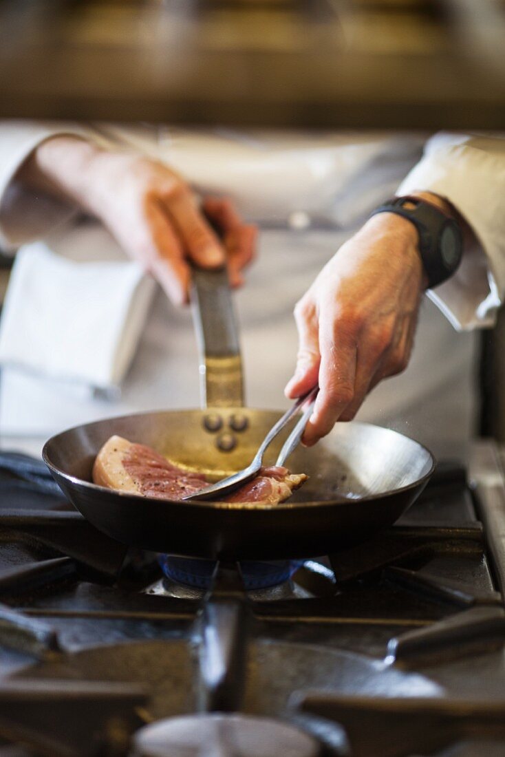 A chef preparing a steak in a commercial kitchen