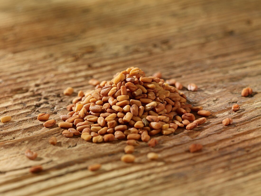 A pile of fenugreek seeds on a wooden surface