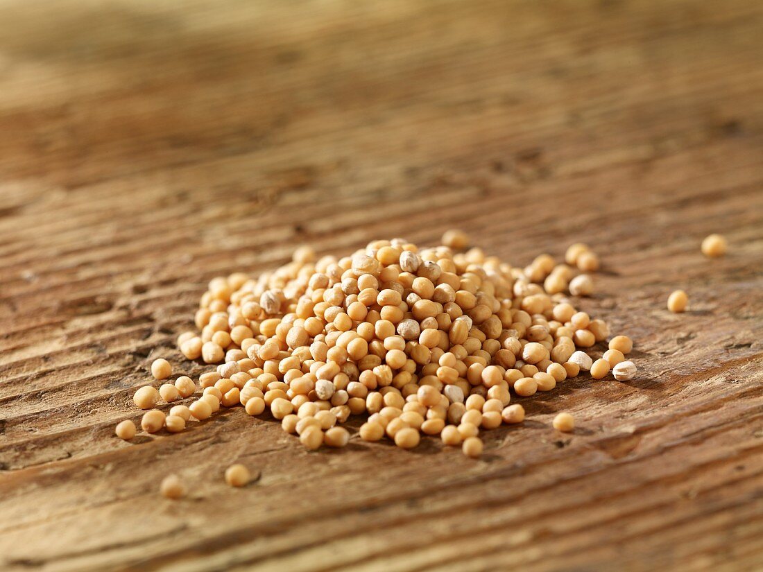 A pile of yellow mustard seeds on a wooden surface