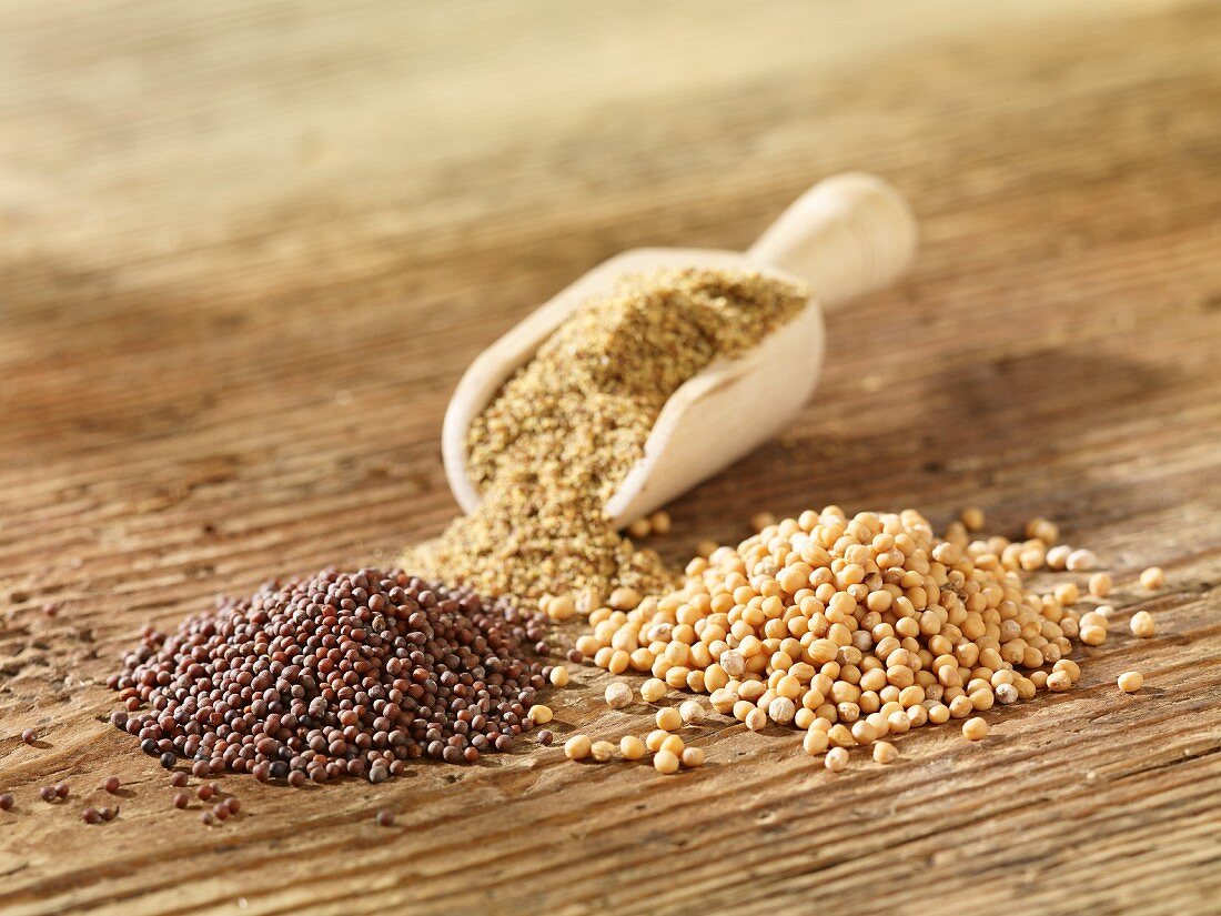 Various mustard seeds on a wooden surface