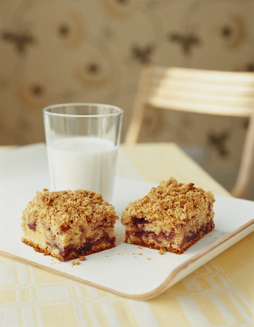 Zwei Stücke Sauerrahm-Streusel-Kuchen mit Johannisbeermarmelade vor Milchglas