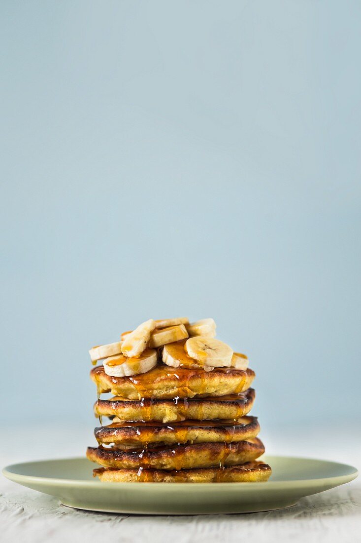 A stack of pancakes topped with banana slices and with dripping maple syrup