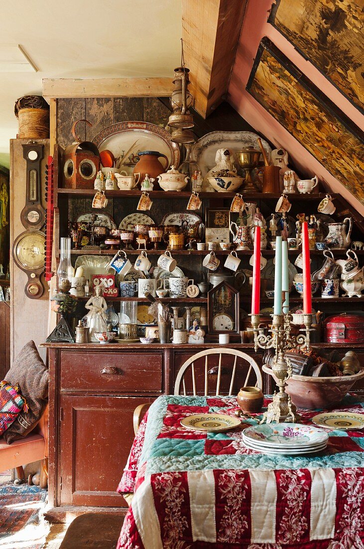 Patchwork quilt and candelabra on table in front of dresser crammed with crockery and flea-market finds