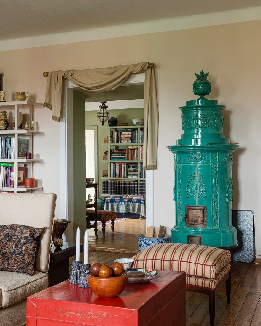 Red, Chinese wooden trunk and stool with striped upholstery in front of antique turquoise tiled stove