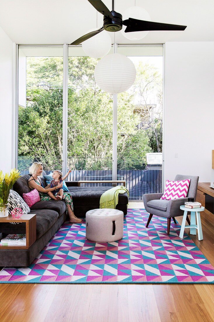 Überecksofa und Retrosessel auf grafisch bunt gemustertem Teppich, hohe Fensterfront zum Garten