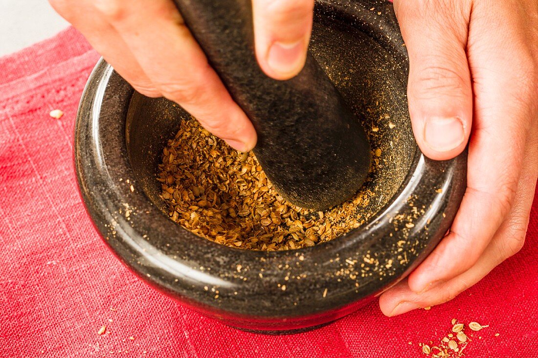 Roasted coriander seeds being crushed in a mortar