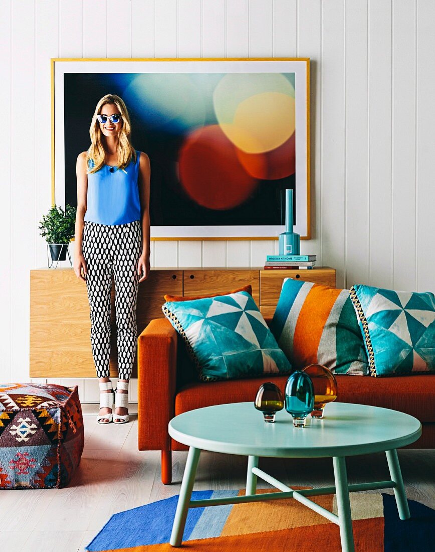 Blue patterned cushions with ethnic print on orange sofa and young woman in sunglasses in front of photo picture