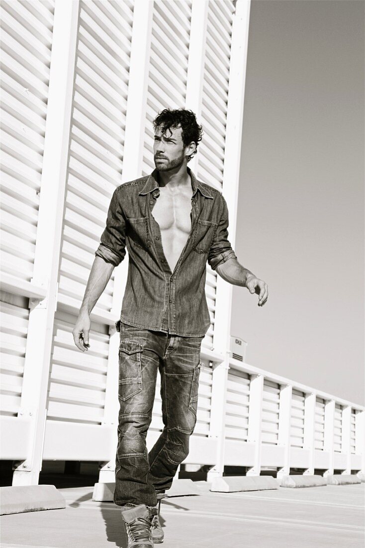 The young man wearing blue jeans and a denim shirt against a white wooden wall (black and white shot)