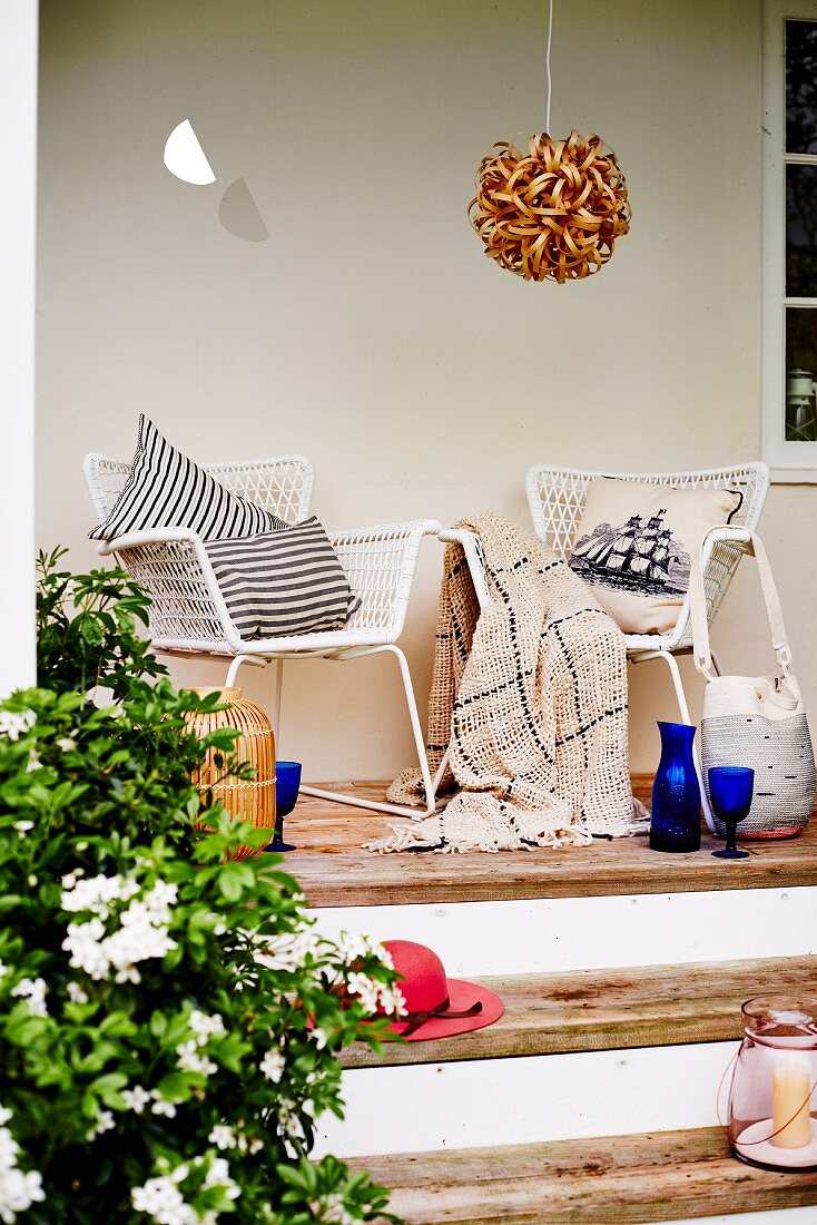 White mesh armchairs with cushions on narrow terrace with wooden steps and spherical rattan pendant lamp