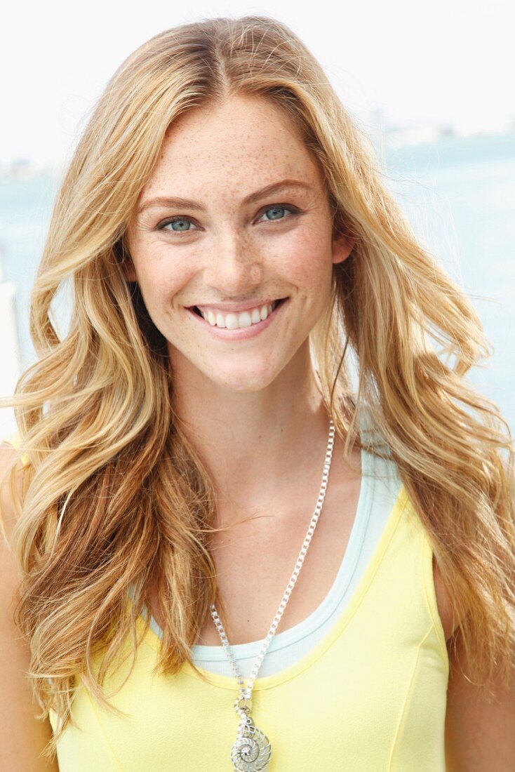 A blonde woman wearing a light yellow top and a fashionable necklace