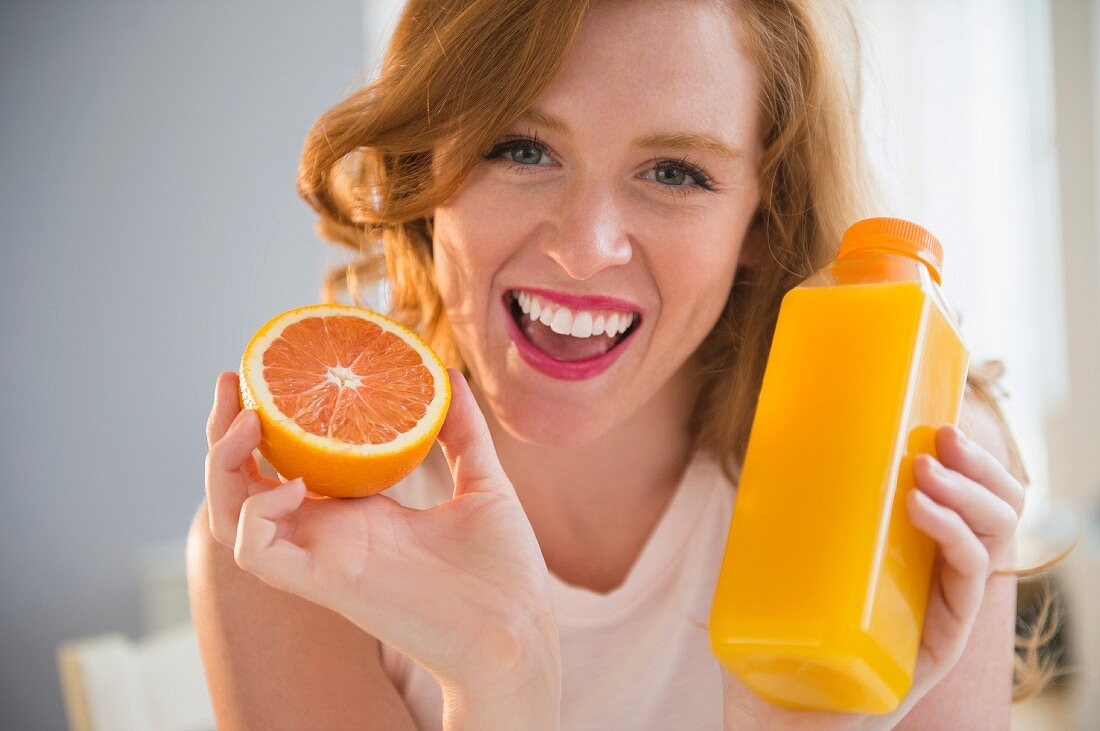 A woman holding an orange and a bottle of orange juice