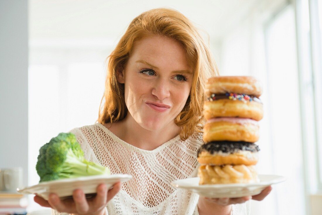 A young woman holding plates of doghnuts and broccoli