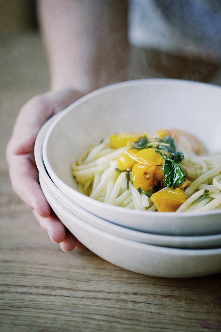 A hand holding a bowl of pasta with tomatoes and goat's cheese