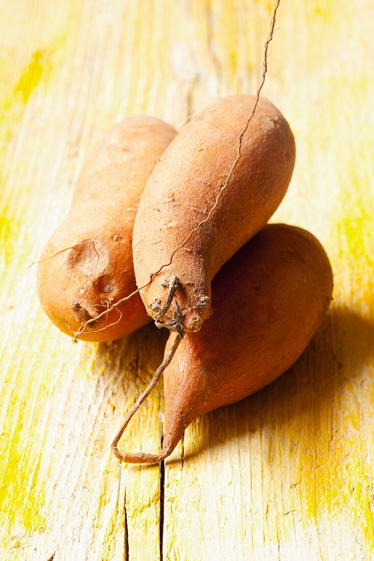 Three sweet potatoes on a wooden surface