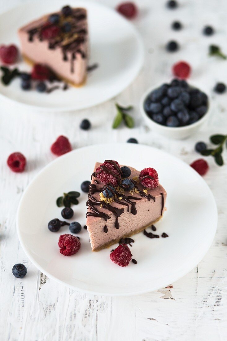 Zwei Stücke Himbeer-Käsekuchen mit frischen Himbeeren, Blaubeeren und Schokoglasur