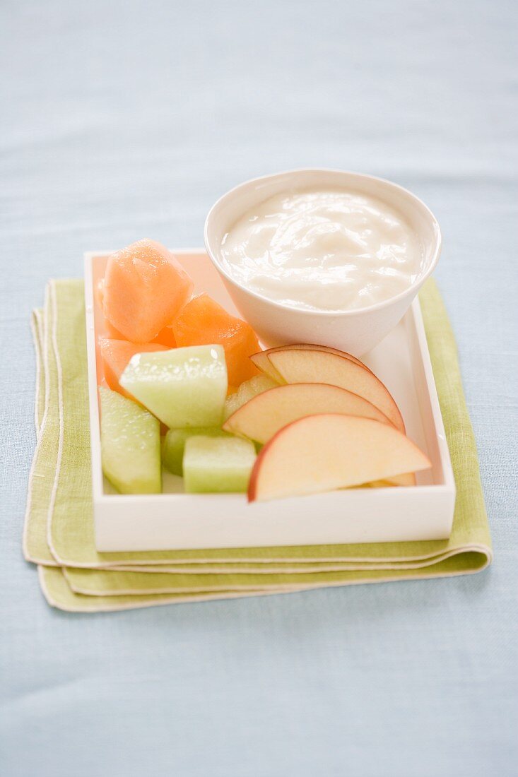 Pieces of melon and apple wedges with a bowl of yoghurt