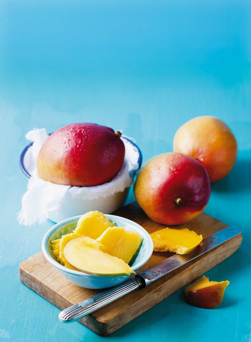Mangos, whole and slices on a blue surface