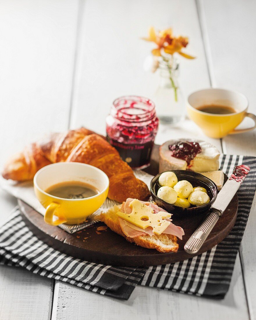 A breakfast platter with croissant, cheese, jam, butter and coffee