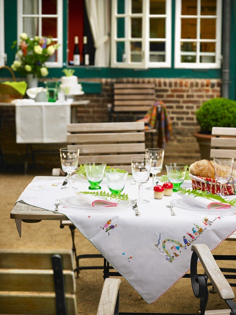 Bestickte Tischdecke auf gedecktem Gartentisch mit Weingläsern auf der Terrasse