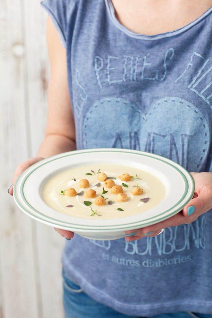 A woman holding a plate of celeriac and potato cream soup with horseradish