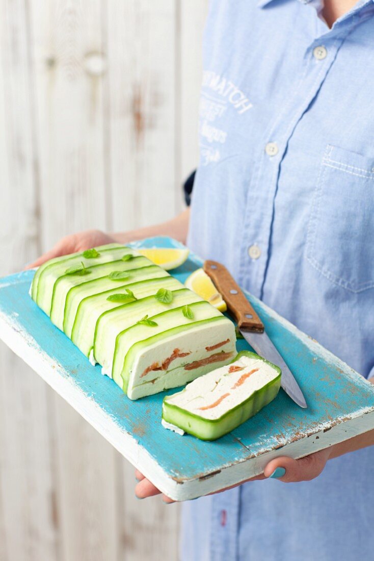 Frau hält Schneidebrett mit Quark-Lachs-Terrine mit Gurken