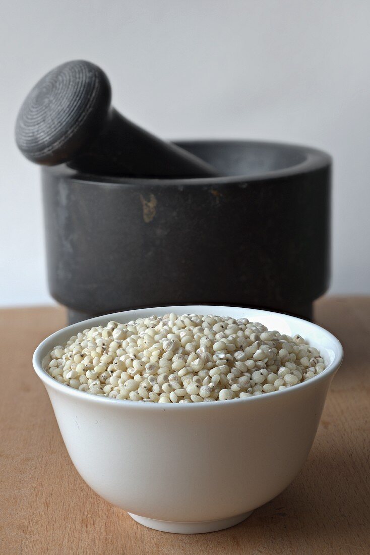 Sorghum in a porcelain bowl in front of a mortar