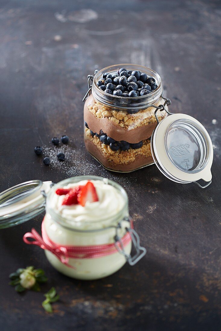 A jar of chocolate mousse with crumbles and blueberries and a jar of white mousse