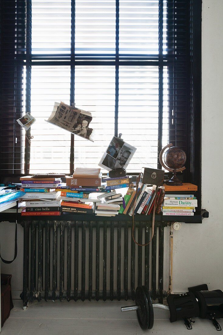 Mit Büchern überladene Fensterbank vor halbgeschlossener Jalousie am Fenster