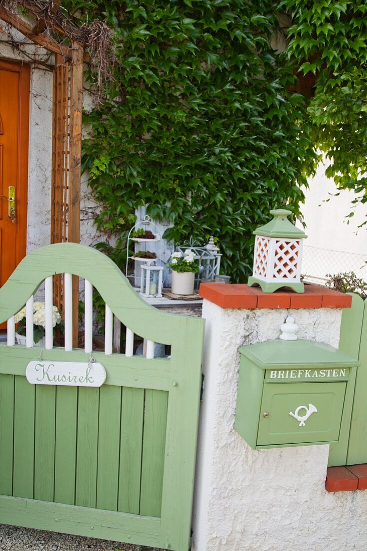Grün lackiertes Holz Gartentürchen, neben Mauerstück mit aufgehängtem Briefkasten in gleicher Farbe