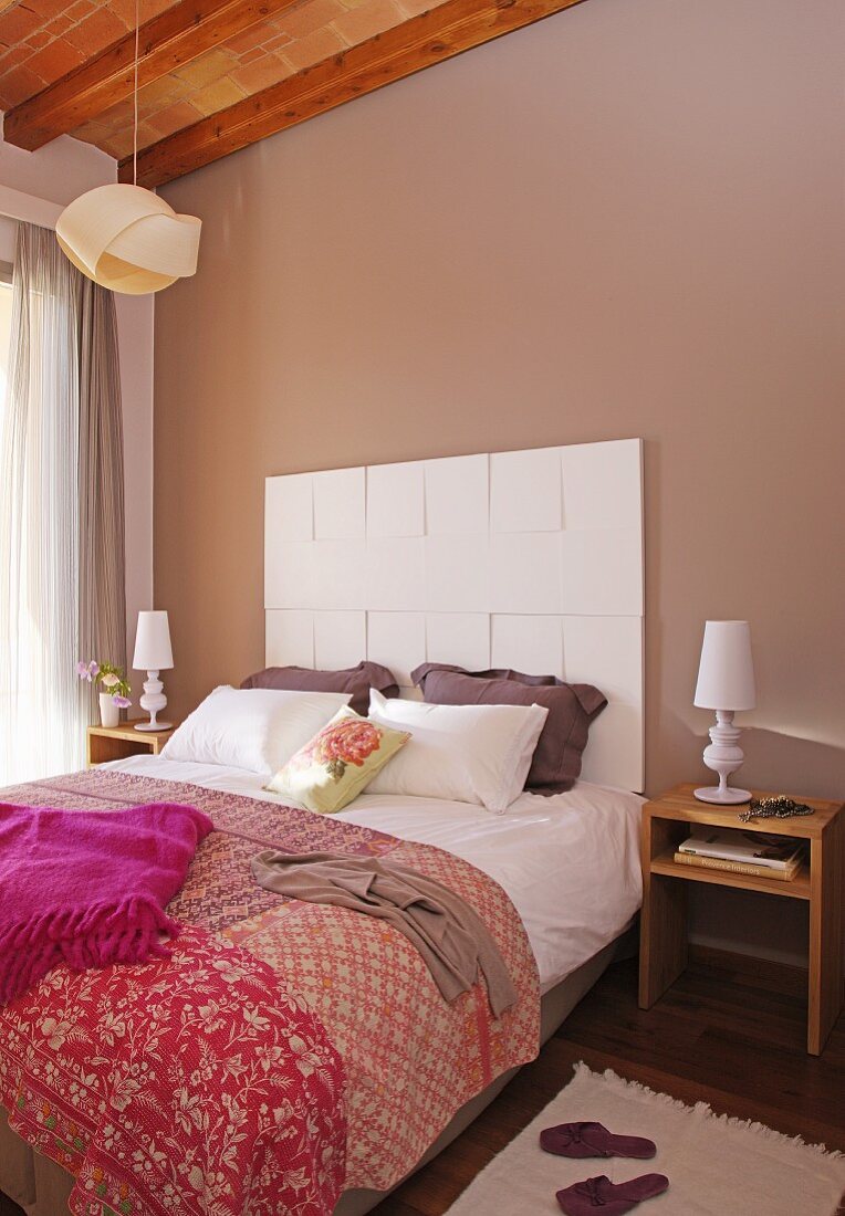 Gemusterte Tagesdecke im Patchworkstil auf Doppelbett, vor weissen Paneelen an pastell brauner Wand in Schlafzimmer