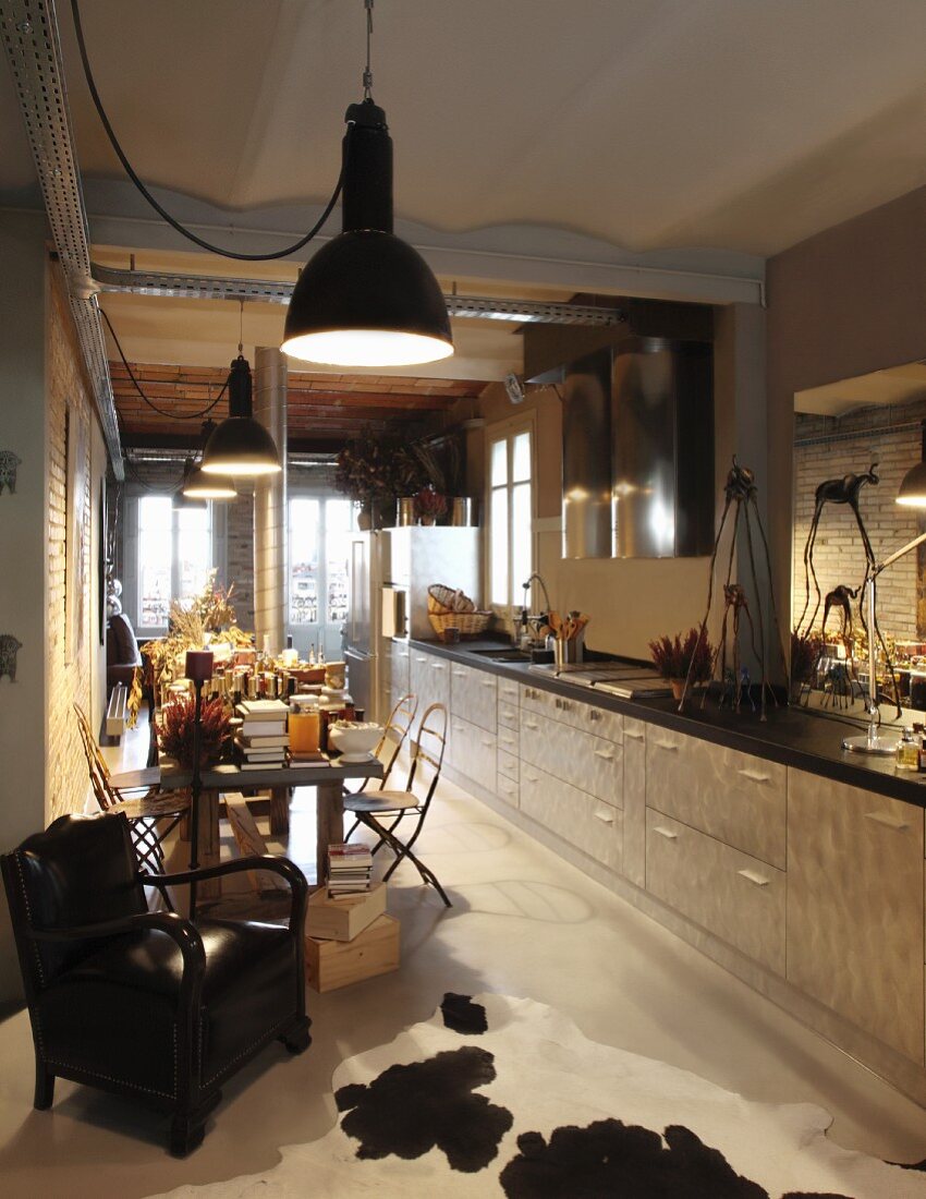 Kitchen counter along entire wall and dining area below row of vintage pendant lamps in open-plan interior