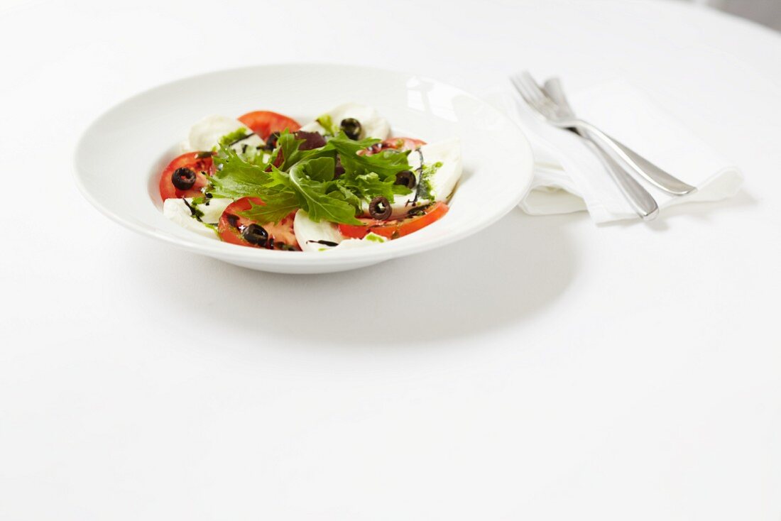 Mozzarella and tomato salad with olives, balsamic vinegar and a pesto dressing