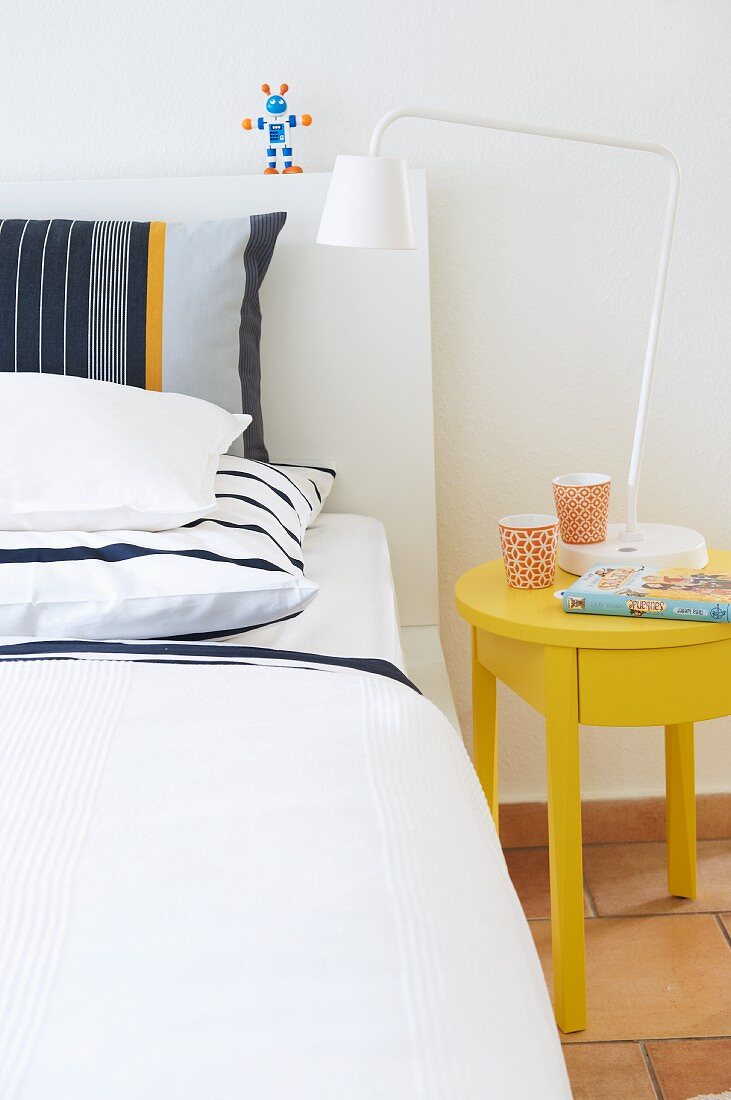 Striped pillows on white bed next to sunshine yellow bedside table