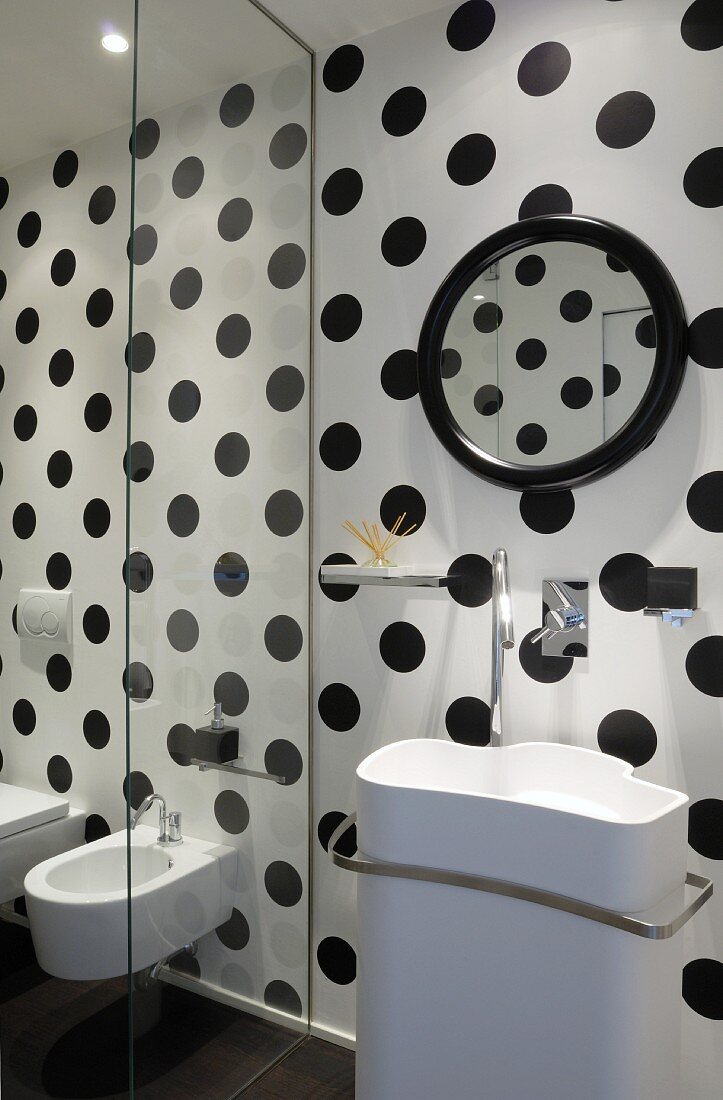 Designer washbasin on black and white polka dot wall; glass panel screening bidet and toilet