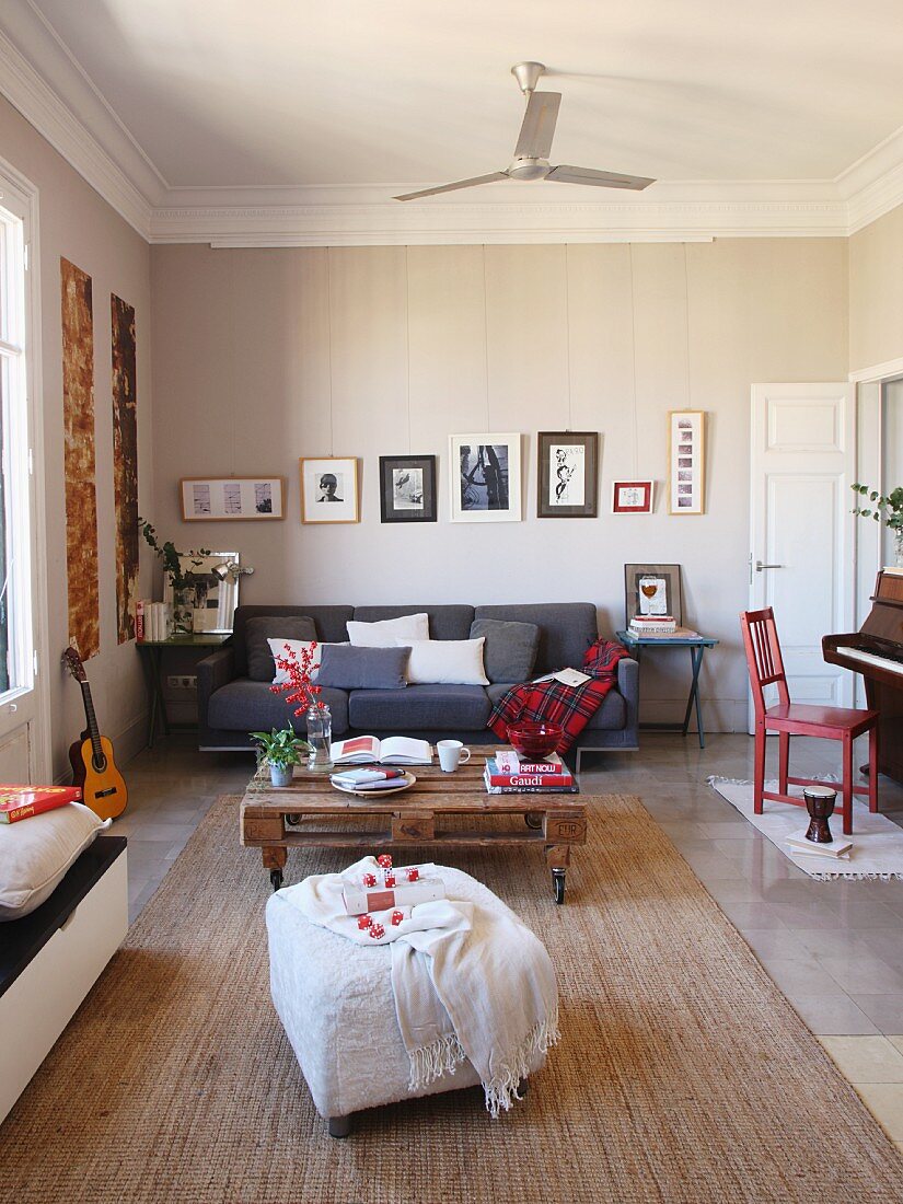 Lounge area with white ottoman, coffee table made from pallet and grey couch in open-plan interior with traditional ambiance