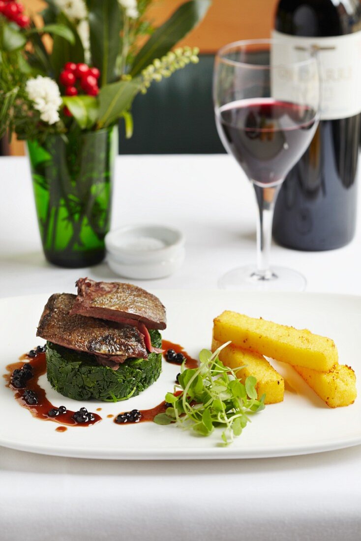 Roast lamb on a spinach timable with polenta sticks and blackcurrant jus