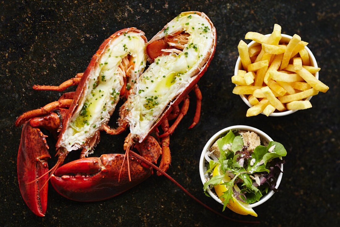 A halved lobster served with chips and a side salad