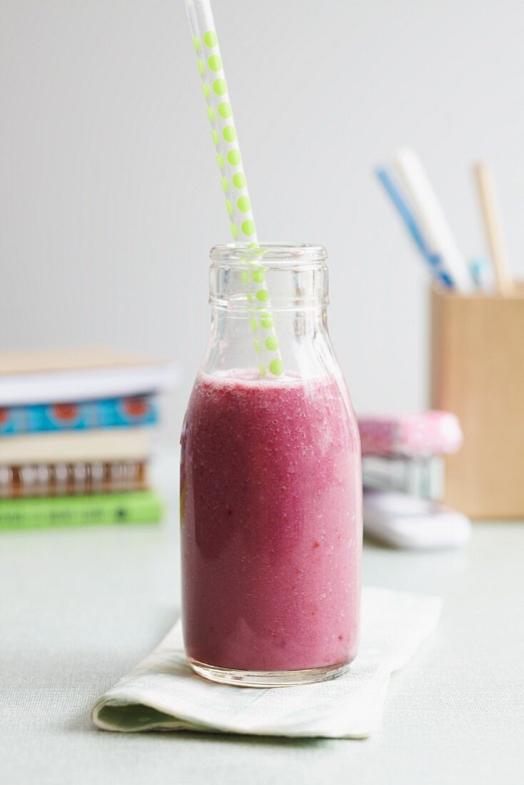 A berry smoothie in a milk bottle with a straw