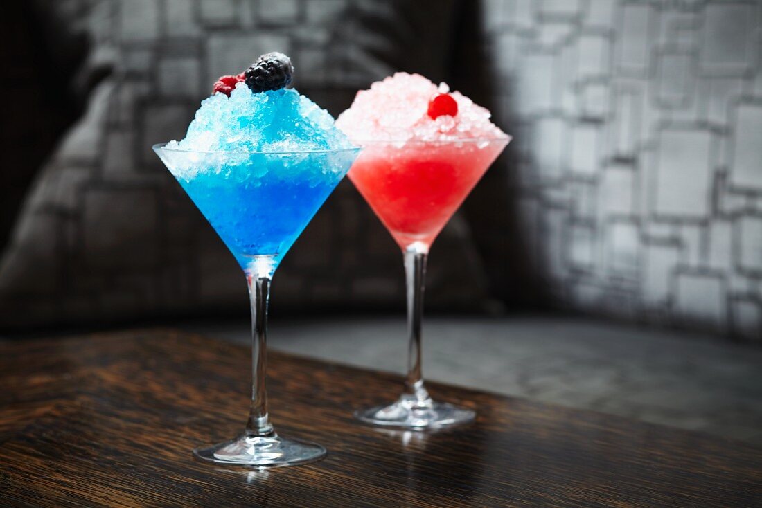 Bright blue and pink frozen cocktails topped with berries and maraschino cherries
