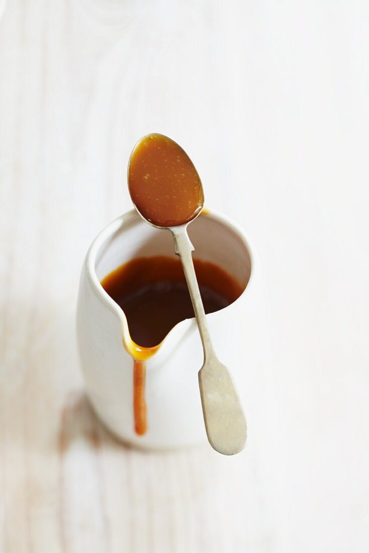 Caramel sauce in a white porcelain jug with a spoon