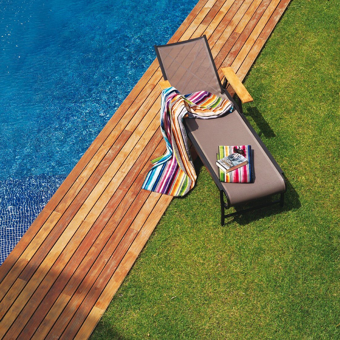 Lawn and wooden deck edging pool; brightly striped towels on modern sun lounger