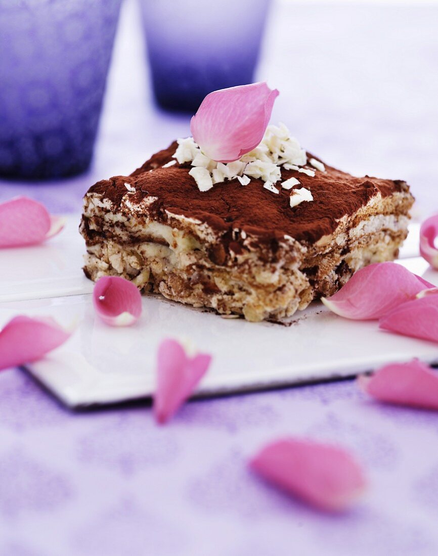 Ein Stück Tiramisù mit weissen Schokoladenraspeln und Rosenblütenblättern garniert